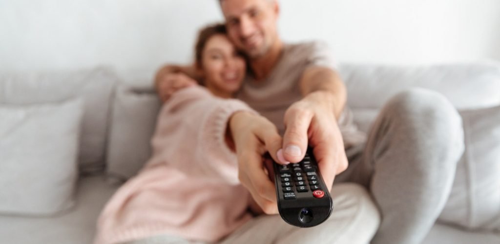 Pareja apuntando con el mando de la tele. Qué ver en la televisión el 24 de marzo?