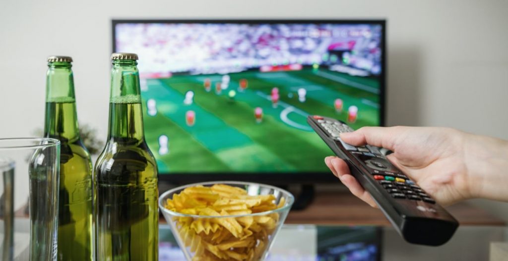 Botellines de cerveza, patatas fritas y un mando apuntando a la televisión.¿Qué ver en la tele el 27 de marzo?