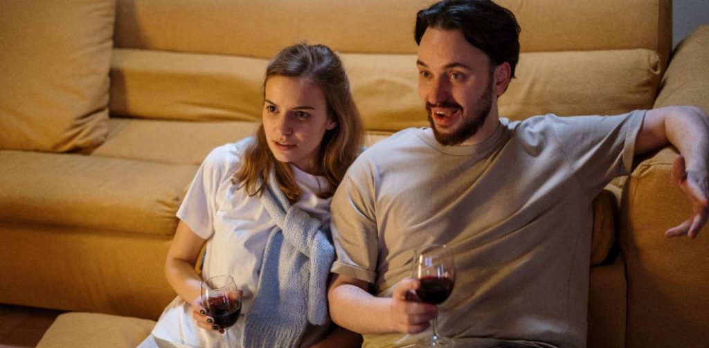 Hombre y mujer ven la televisión mientras beben una copa de vino el 29 de marzo