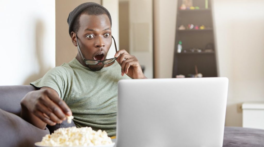 Hombre sorprendido come palomitas mientras ve la tele en el ordenador el 14 de abril