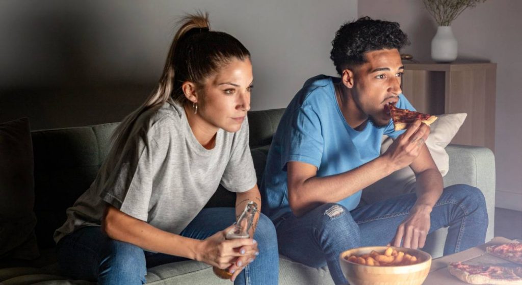 Hombre y mujer comen pizza y beben cerveza mientras ven la televisión el 24 de abril