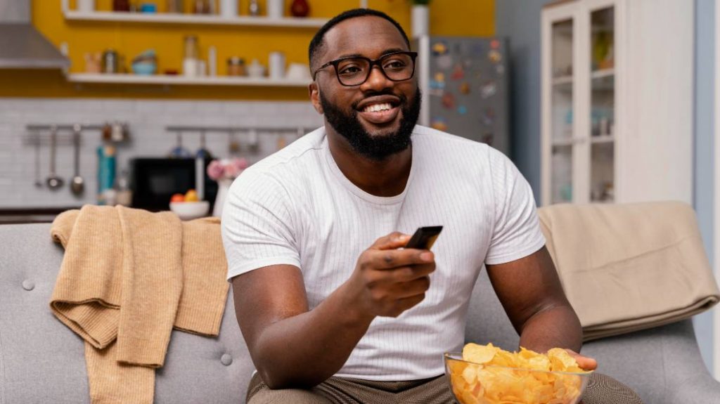Hombre come patatas fritas y ve la televisión el 25 de abril