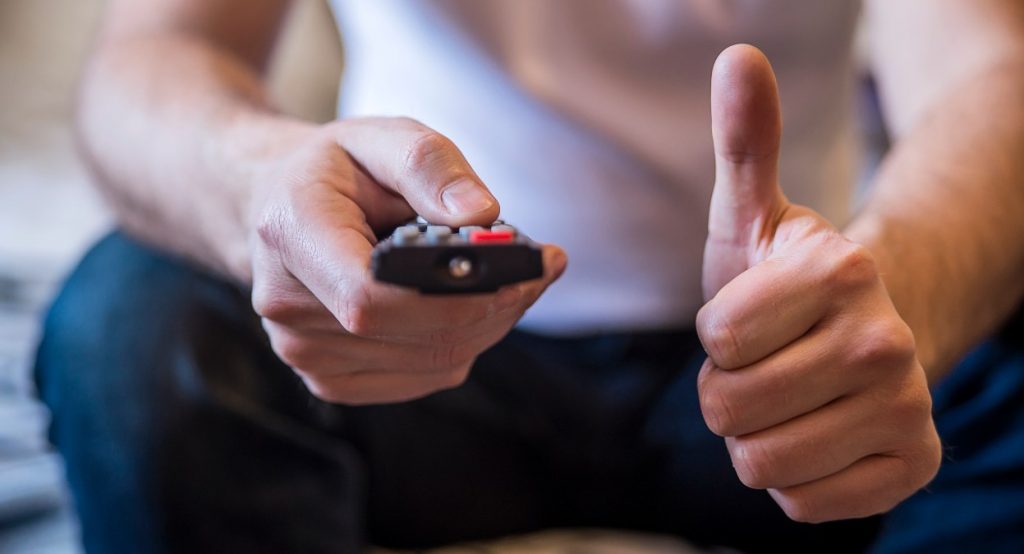 Hombre sosteniendo un mando y levantando el pulgar mientras ve la televisión el 27 de abril