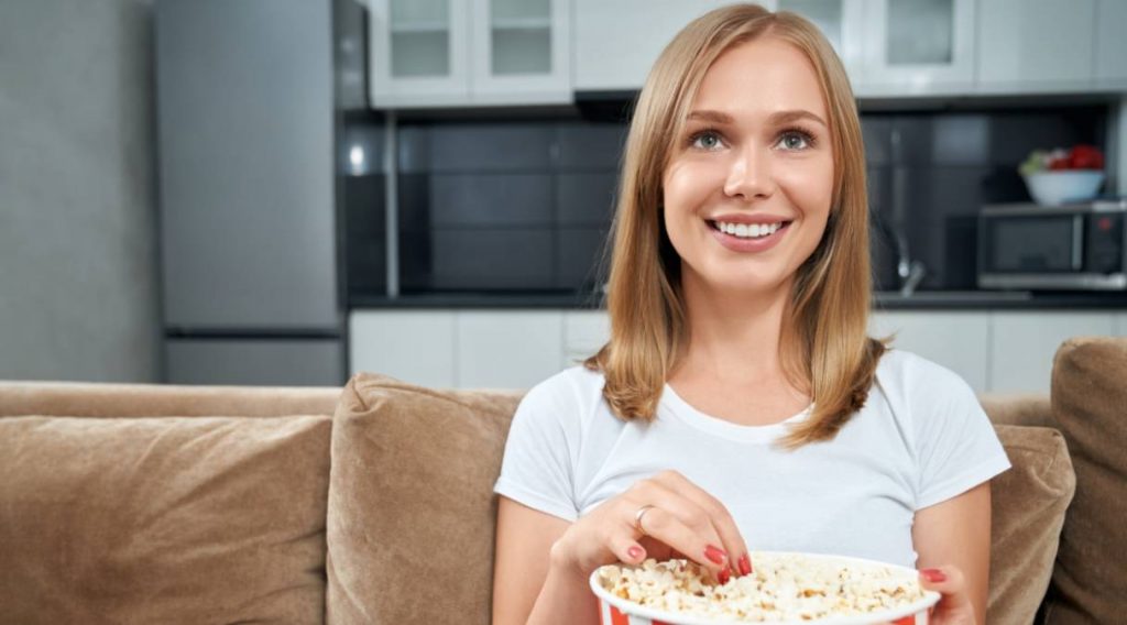 Mujer joven ve la tele y come palomitas el 25 de junio